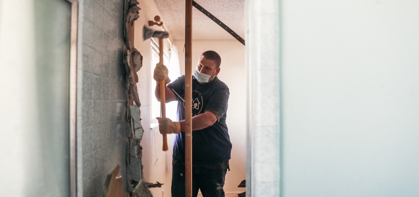 A volunteer uses an axe to tear down a bathroom wall.
